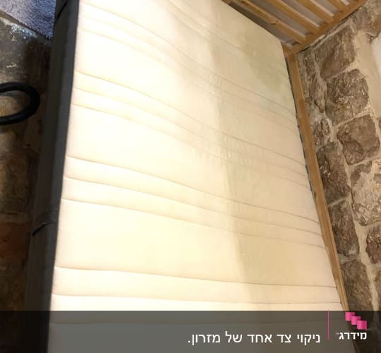מזרן לבן עם כתמים על מסגרת עץ